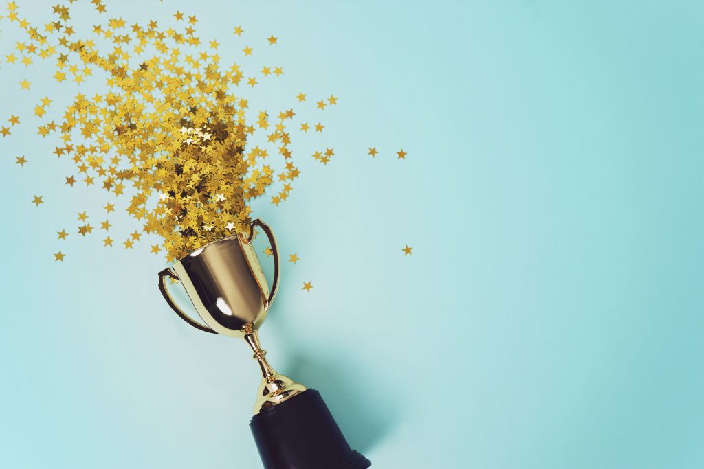 a trophy with gold stars coming out of the top on a teal background