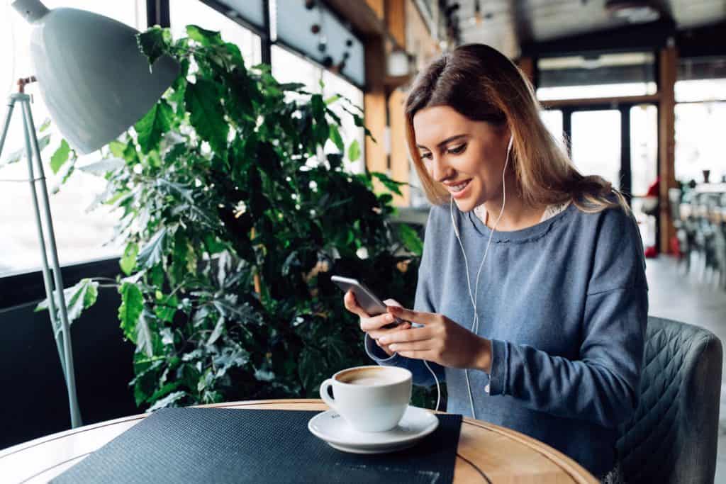 woman in gray shirt looking at social media on her smartphone in a coffee shop