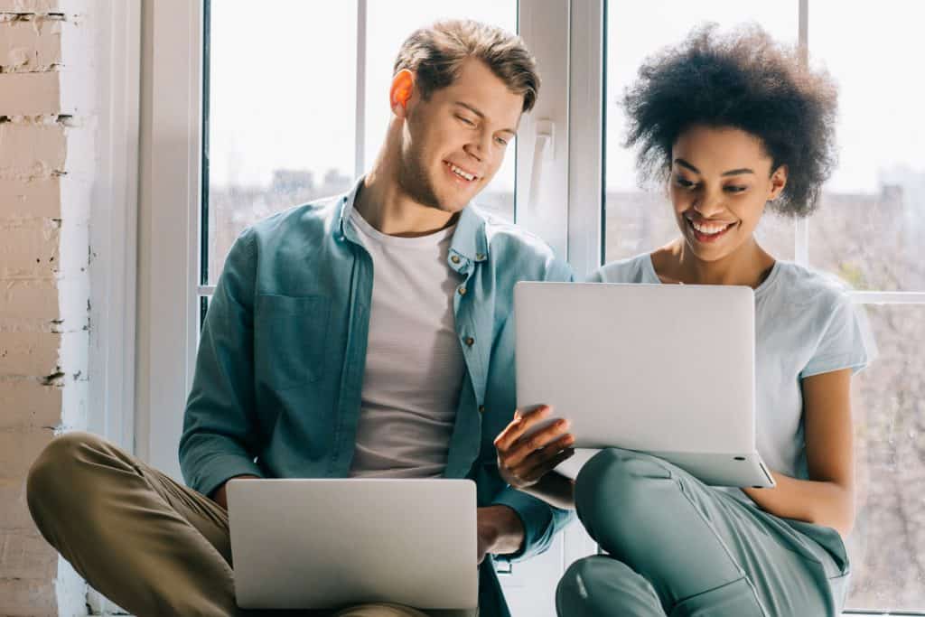 couple sitting in against an apartment window working together on their laptops