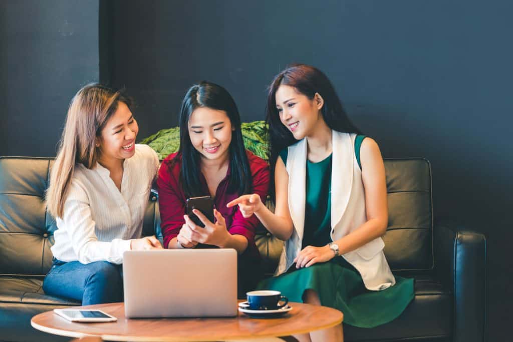 three female bloggers looking at a smartphone and a laptop together on a couch