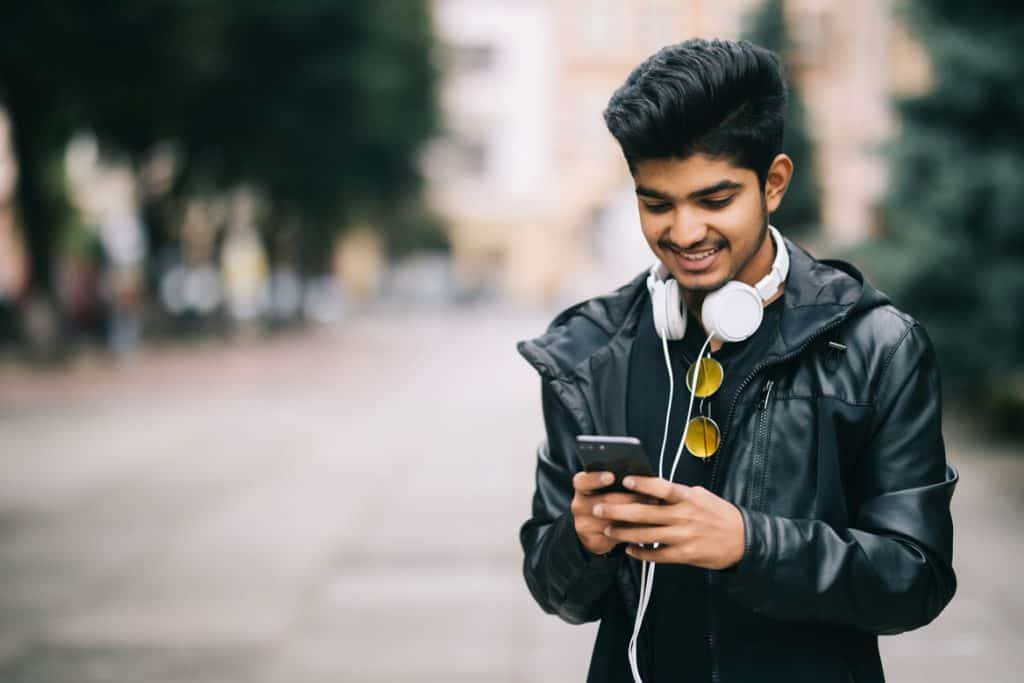 male blogger in leather jacket typing on his cell phone while walking on an empty street